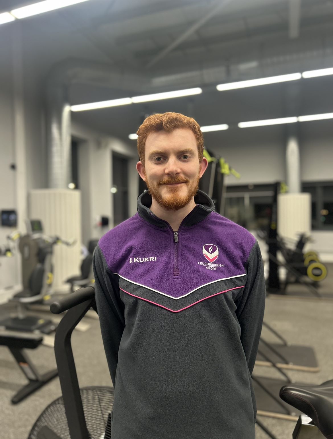Fitness Coach, Luke, standing in front of an exercise bike smiling.